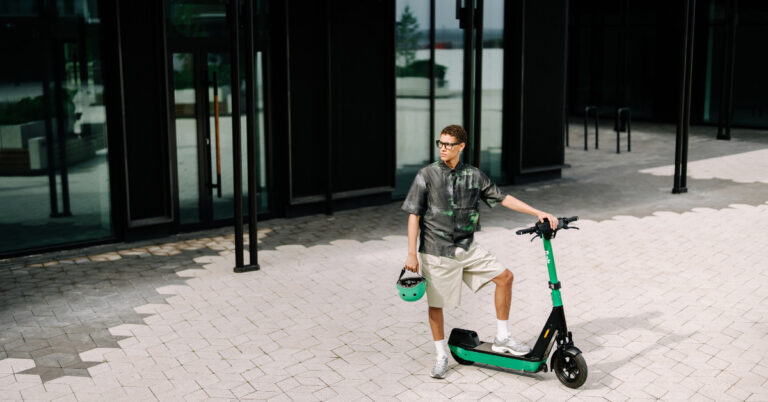 A young man standing next to a Bolt scooter and holding a helmet